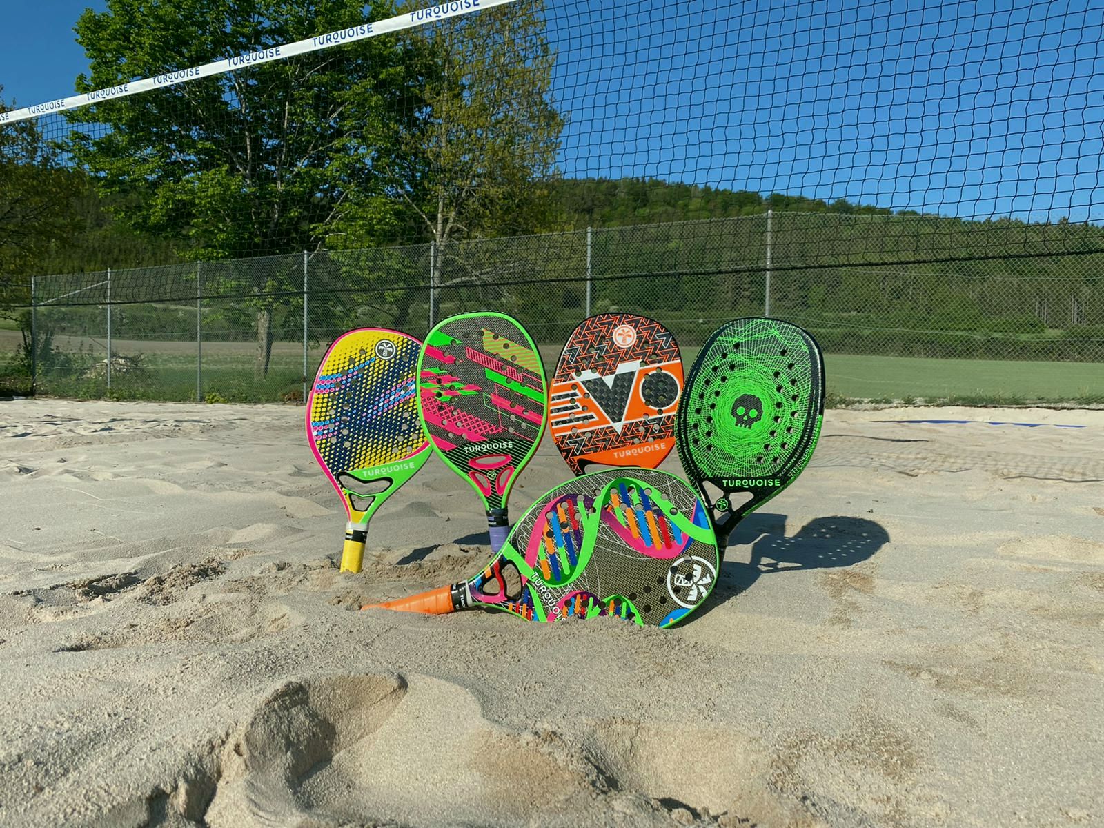 Fünf bunte Beach-Tennis-Schläger im Sand vor dem Netz