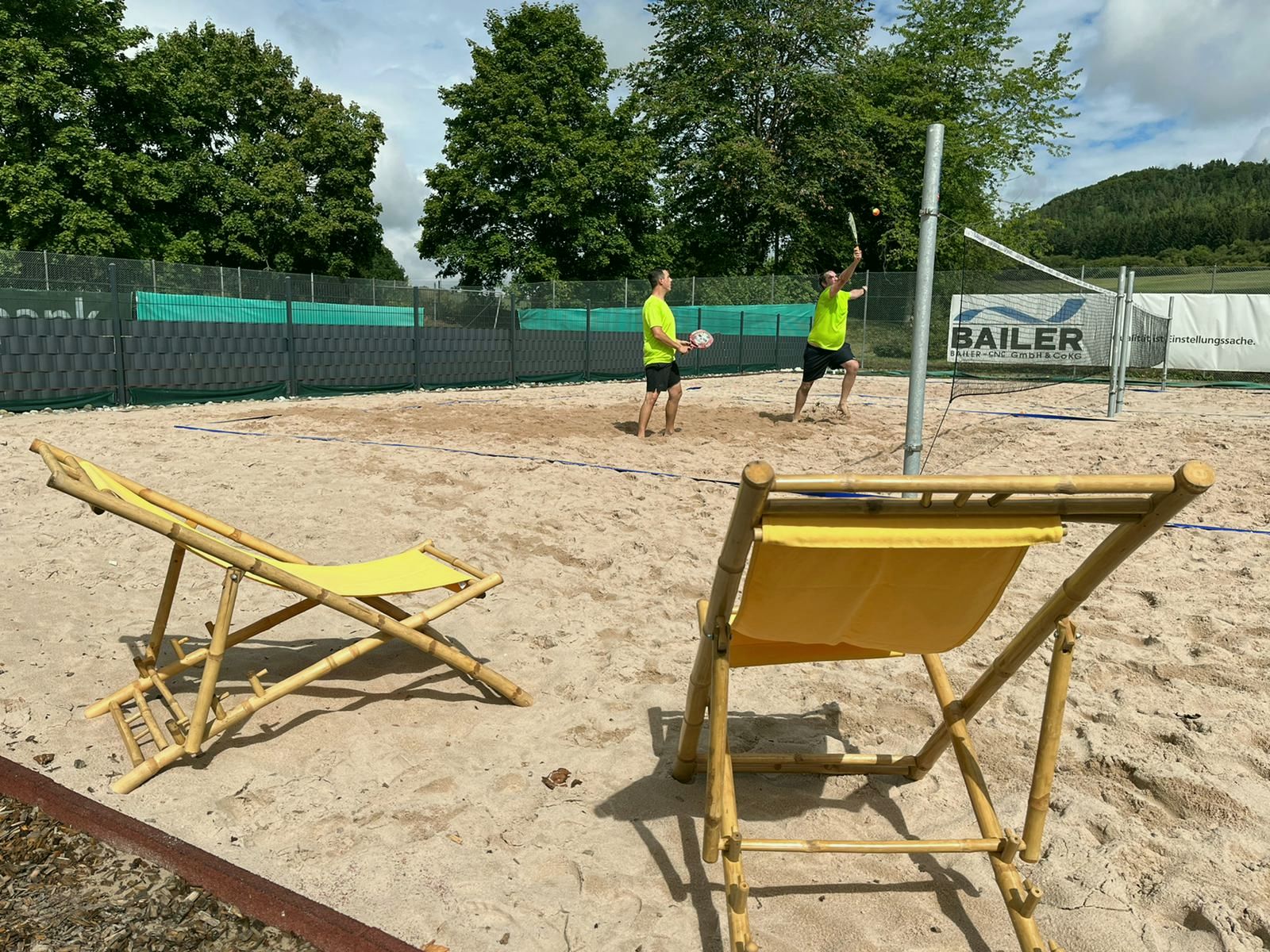 Zwei Spieler im Doppel, im Vordergrund zwei gelbe Liegestühle